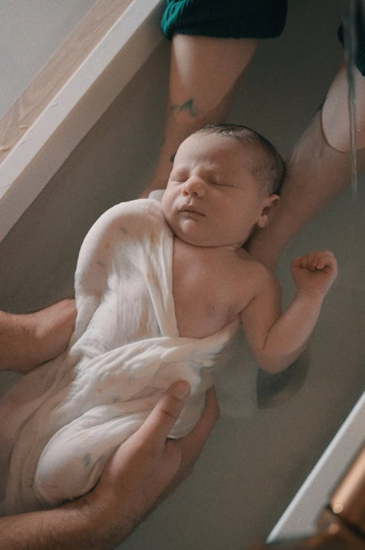 Nouveau-né emmailloté dans un lange, tenu dans le bain thérapeutique